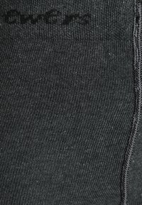 Chaussette noire côtelée avec une texture lisse. Comprend un petit logo imprimé sur le dessus et dispose d'une couture de renfort au niveau des orteils pour plus de durabilité.