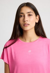 Maglietta sportiva rosa a maniche corte con scollatura rotonda, caratterizzata da un leggero motivo testurizzato e un logo bianco sul petto.