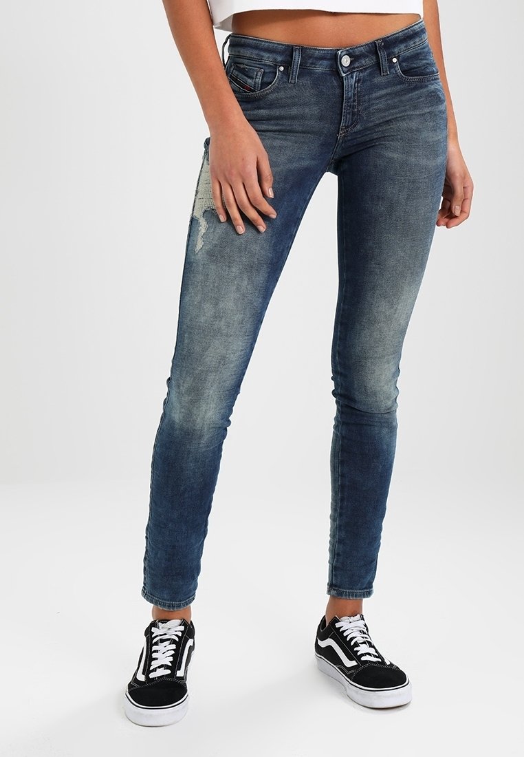 Oblečení úzké džíny ve středně modré barvě, s popraskanou záplatou, pěti kapsami a kovovými detaily. V kombinaci s černobílými teniskami.