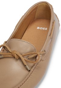 Mocassin beige en cuir avec lacet en daim noué en nœud, détails cousus et « BOSS » imprimé à l’intérieur de la semelle.