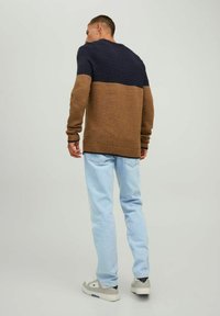 Pull en maille marron et bleu marine, motif texturé en haut, corps lisse, col rond, poignets côtelés, associé à un jean bleu clair et des baskets.