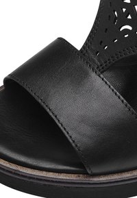 Sandal in pelle nera caratterizzata da una larga fascia orizzontale, un motivo ritagliato sulla parte superiore e una suola testurizzata. Soletta sottile con cuciture a contrasto.