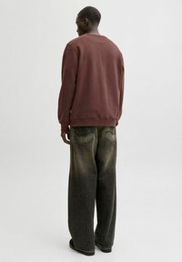 Brown sweatshirt with a relaxed fit, paired with oversized, faded black jeans featuring back pockets and a straight leg design.