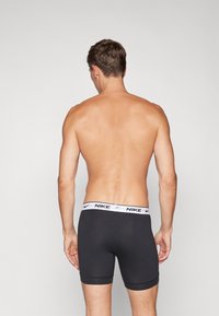 Boxers Nike negros con una cinturilla blanca con la marca, diseño ajustado y bordes sin costuras, vistos desde atrás. Textura de tela suave visible.
