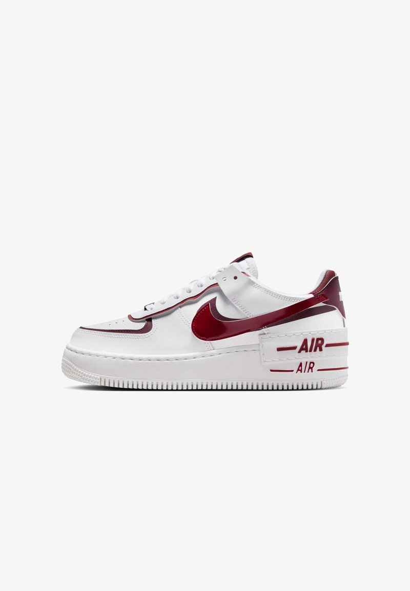 Hvid Nike Air Force 1 sneaker med røde detaljer. Har en glat læderoverdel, perforeret tåboks og en tyk gummisål med "AIR" detalje.