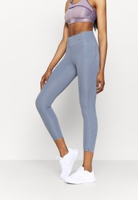Jasnoniebieskie legginsy sportowe o dopasowanym kroju, z bocznymi zamkami i gładką teksturą, zestawione z dopasowanym fioletowym biustonoszem sportowym.