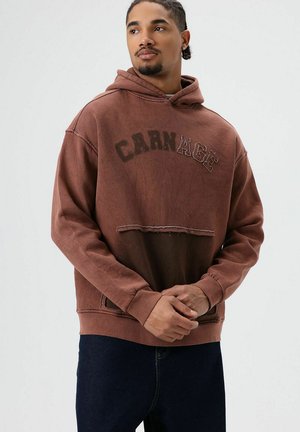 Sweat à capuche marron surdimensionné avec un ourlet court et des lettres usées "CARNAGE". Confectionné en matière douce avec une coupe décontractée et une poche avant.