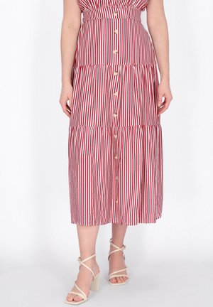 Frau trägt einen rot-weiß gestreiften Midirock mit senkrechten Streifen und Knöpfen vorne, kombiniert mit beigefarbenen, Riemchen-Sandaletten mit hohen Absätzen.