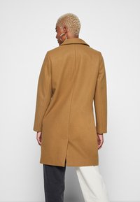 Cappotto in misto lana marrone con colletto a revers, maniche lunghe e uno spacco posteriore. Il design presenta una vestibilità sartoriale con linee pulite e minimaliste.