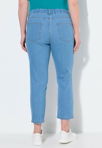 Světlé modré džínové kalhoty s tapered nohavicemi, elastickým pasem a dvěma zadními kapsami. Oblékané s bílými teniskami a teal topem.