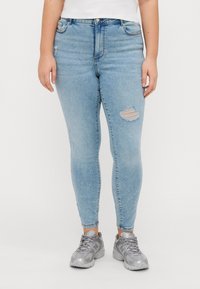 Light blue high-waisted skinny jeans with whiskering and a knee rip, paired with gray athletic sneakers. Denim fabric has a smooth texture.