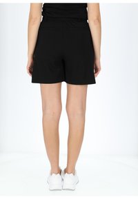 Sorte shorts lavet af blødt stof, med en glat tekstur, enkelt design og to baglommer, parret med hvide sneakers.