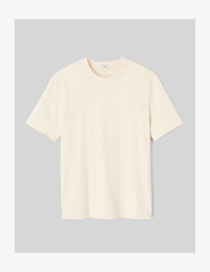 Chemise crème à manches courtes avec une écharpe à motifs, shorts noirs et mocassins noirs brillants. Modèle posant devant un fond neutre.