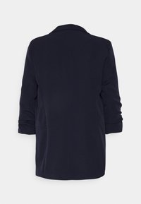 Blazer blu navy di lunghezza media con un design semplice, texture morbida, colletto a scollo a diamante e maniche arrotolate. Presenta due tasche laterali.