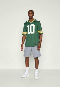 Maillot de football vert avec le numéro 10 en blanc et des rayures jaunes sur les manches, associé à un short gris clair et des baskets blanches.