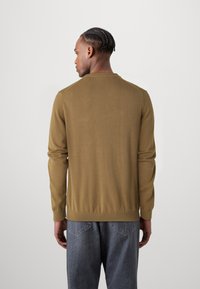 Pull en tricot marron à manches longues, avec un ourlet côtelé et un col rond, assorti à un jean gris, vu de dos. Texture lisse, design minimaliste.