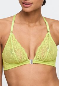 Bralette en dentelle vert citron avec des bonnets triangulaires, des bretelles en soie et une fermeture métallique à l'avant. Présente des motifs floraux élaborés.