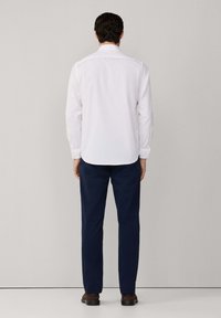 Camisa blanca de manga larga con cuello abotonado, combinada con pantalones azul marino de corte recto y una sutil textura.