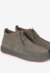 Stivaletti chukka in suede grigio con lacci grigi, accenti rossi a contrasto e una fodera interna testurizzata. Suola nera spessa con suola rossa.