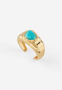 Anello a cucchiaio in tono oro con una superficie liscia e lucida e una pietra di turchese triangolare incastonata in una fascia ondulata e testurizzata.