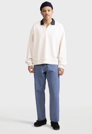 Cream pullover sweatshirt with a green collar, paired with light blue straight-leg jeans and black shoes. Simple and relaxed fit.
