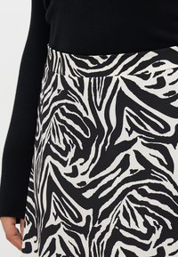 Svart og hvitt skjørt med zebra trykkmønster, med en glatt tekstur og en tettsittende midje. Delvis synlig svart gensererm.