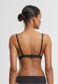 Črn bralette z nastavljivimi naramnicami in zaponko. Gladka tekstura, minimalističen dizajn. Vključuje subtilen šiv in podporno strukturo.