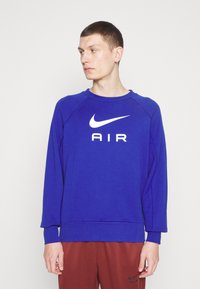 Nike plava dukserica s bijelim "AIR" logotipom i swoosh oznakom. Ima okrugli izrez, duge raglan rukave i opušteni kroj. Mekana tekstura.