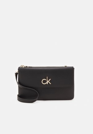 Zwart leren Calvin Klein polstasje met gouden CK-logo en een afneembare riem op een witte achtergrond.