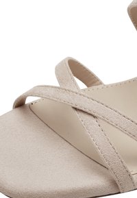 Sandale en suède beige avec des brides croisées et un bout rond lisse. Présente une semelle plate et un détail de couture minimal.