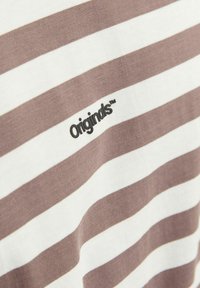 Csíkos póló világosbarna és fehér pamutból, elöl egy kis fekete "Origins™" logóval. Sima textúra, laza dizájn.