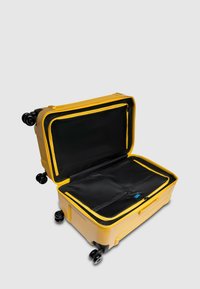 Valise rigide jaune avec quatre roues noires, ouverte pour révéler un intérieur noir et des compartiments zippés. Texture lisse et forme rectangulaire.