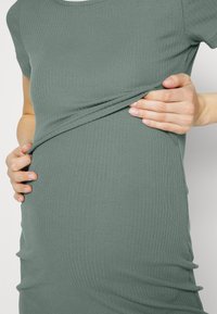 Grön ribbad stickad klänning med rundad halsringning, korta ärmar och kroppsnära passform, som visar ett texturerat tyg och samlade detaljer.