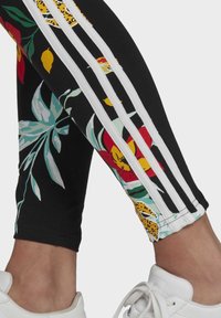 Černé legíny s živými květinovými a leopardími vzory. Nabízejí tři bílé pruhy po stranách. Navrženy s vypasovaným, elastickým materiálem.