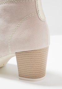 Stivale alla caviglia in suede rosa chiaro con un tacco a blocco texture marrone chiaro e dettagli di cucitura bianca. Design della punta liscia e arrotondata.