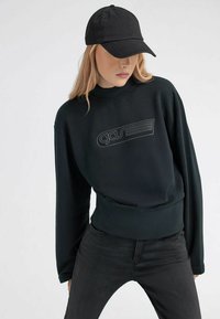 Felpa nera con collo alto, caratterizzata da un design del logo grigio, maniche lunghe e vita aderente, abbinata a un berretto nero coordinato.