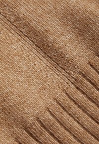 Teksturowana dzianina w jasnobrązowym odcieniu, z prążkowanym wzorem o zmiennej grubości, ukazująca miękkie i ciepłe włókna.