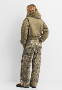 Olivno zelena bomberska jakna z ovratnikom iz krzna, v kombinaciji s hlačami širokega kroja, ki imajo vzorec leoparda. Mehka tkanina, sproščen kroj.