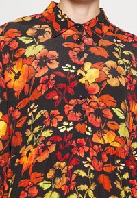 Šaty s květinovým potiskem s výraznými oranžovými, žlutými a červenými květy na černém pozadí. Košilový límec a strukturovaná tkanina.