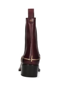 Bottine en cuir bourgogne avec des panneaux élastiques sur les côtés, quincaillerie dorée et un petit talon carré. Texture lisse avec un bout arrondi.
