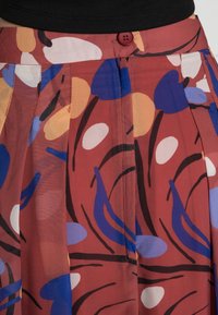 Pleated skirt in a red fabric with a floral pattern in blue, yellow, and white. Features a red button at the waistband.