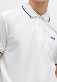 Polo shirt blanc en tissu texturé. Présente un col à rayures noir et gris et un petit logo BOSS sur la poitrine gauche.