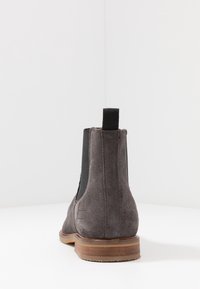 Stivaletto in suede grigio con pannelli elastici laterali, suola in gomma e una piccola linguetta sul retro. Presenta una punta arrotondata e cuciture decorative.