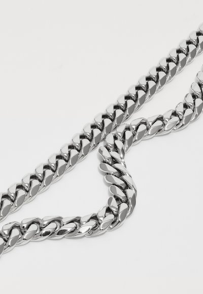Close-up of twisted, polished silver chain links arranged diagonally on a white surface.
