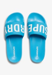 Blauwe slide-sandalen met een brede band met witte "SUPERDRY"-tekst. Glad oppervlak, strak ontwerp en gevormde voetbed voor comfort.