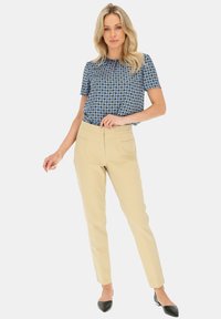 Kobiecy strój z niebieską, wzorzystą bluzką z krótkim rękawem i beżowymi, dopasowanymi spodniami, dopełniony czarnymi butami na szpic.