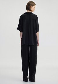 Black oversized blouse with short sleeves, smooth texture, and a collar, paired with matching loose-fitting black pants.