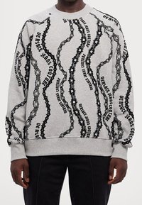Sudadera gris con estampado de texto y cadena negra en patrón ondulado, con puños y dobladillo acanalados para un ajuste ceñido.