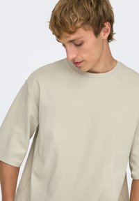 T-shirt en coton beige avec un col rond et des manches courtes, présentant une coupe décontractée et une texture lisse. Design minimaliste sans motifs.