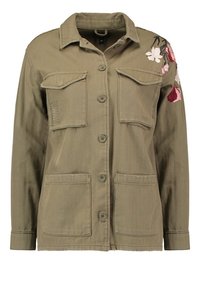 Olivově zelená bunda vyrobená z bavlněné směsi. Má dvě náprsní kapsy, dvě spodní kapsy a květinovou výšivku na pravém rameni.
